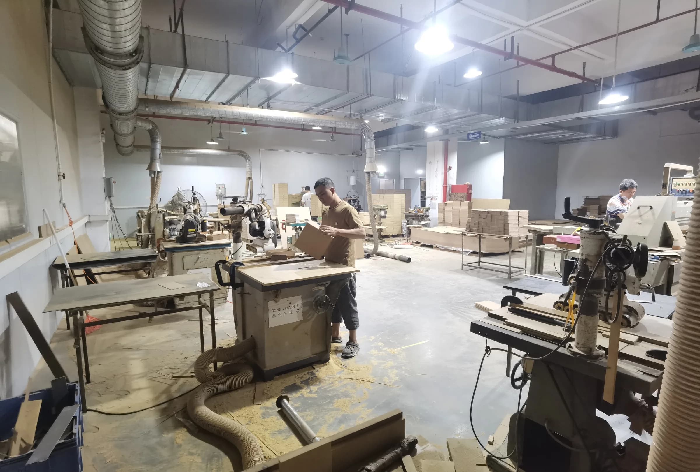 Material preparation workshop with machinery, extraction ducts and an employee handling a board